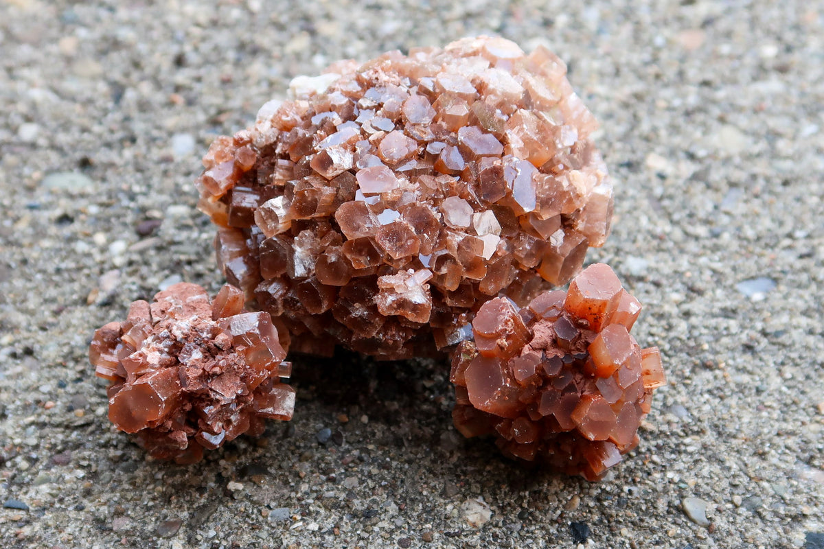 Three clusters of brown translucent gemstone crystals, resembling sugar cubes, resting on a textured gray concrete surface.