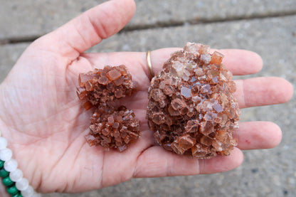 A close-up of a person's hand holding three clusters of brown translucent gemstone crystals against a blurred concrete background.