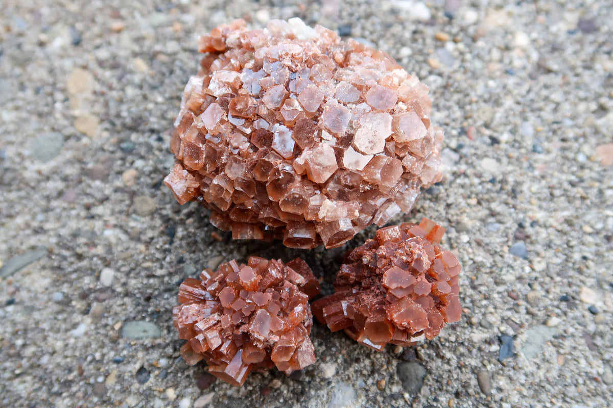 Three clusters of rough, crystalline brown salt or mineral specimens placed on a gray gravel surface.