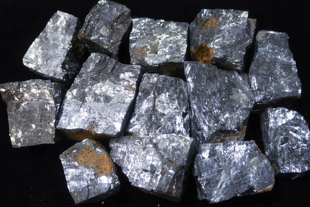 A pile of rough, metallic silver-gray mineral chunks with small brownish-orange inclusions, photographed against a solid black background.