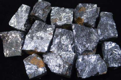 A pile of rough, metallic silver-gray mineral chunks with small brownish-orange inclusions, photographed against a solid black background.