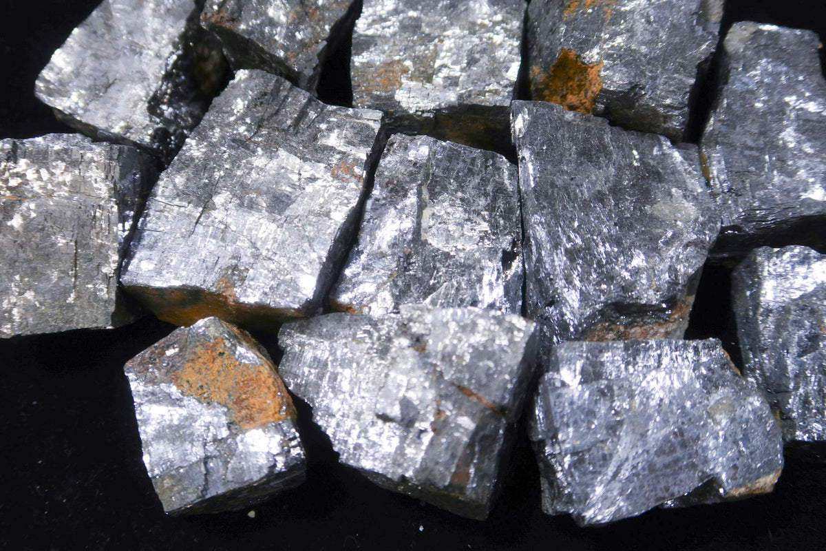 A pile of rough, metallic gray mineral chunks with silver and bronze flecks, set against a solid black background.