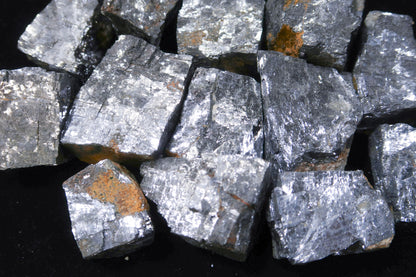 A pile of rough, metallic gray mineral chunks with silver and bronze flecks, set against a solid black background.