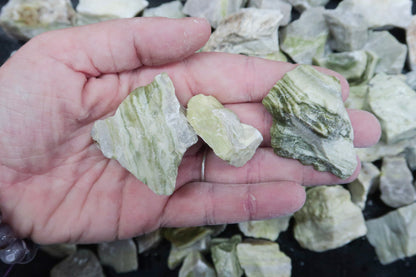 Close up picture of a hand holding rough yellow serpentine stones approximately 1-2 inches in size