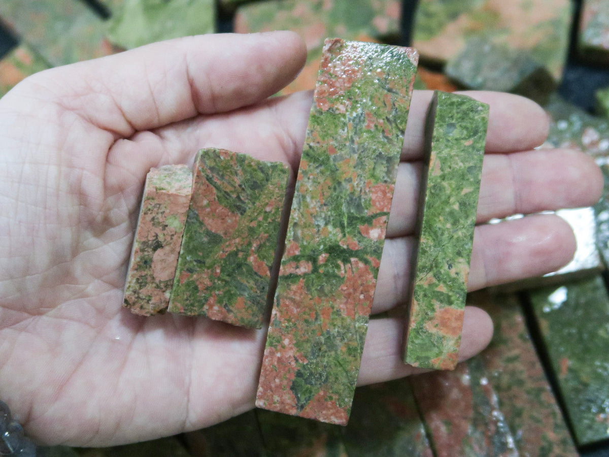 Close up picture of a hand holding rough unakite stones cut into rectangular pieces. 